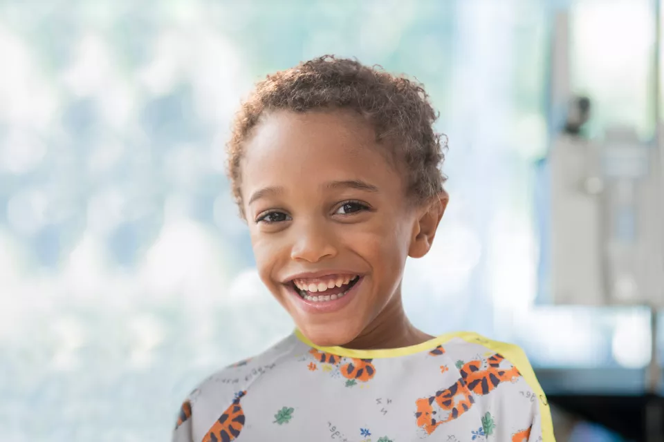 A medium-dark skin toned boy smiles. He is wearing hospital pajamas with tigers on them.