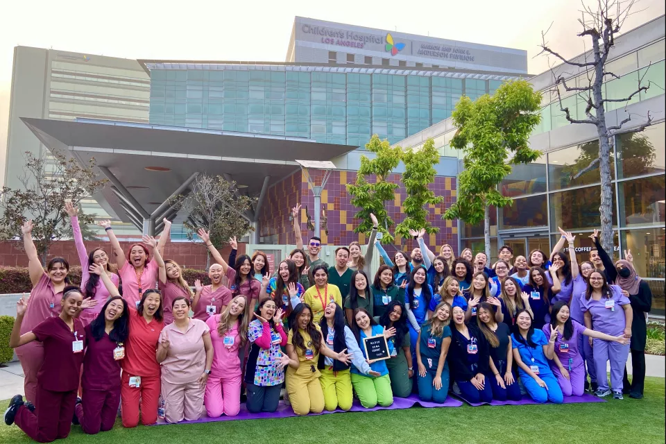 Group photo of over 50 adults wearing colorful, color-coordinated nurses' uniforms posing outside the CHLA main campus building