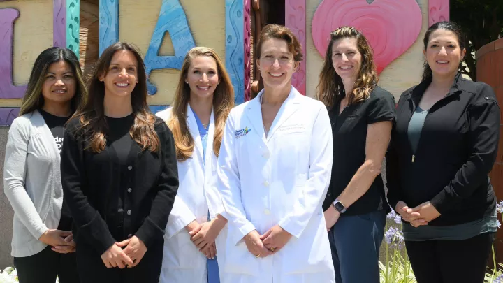 Four smiling women dressed in business attire flank two female doctors wearing white lab coats in front of Children's Hospital Los Angeles