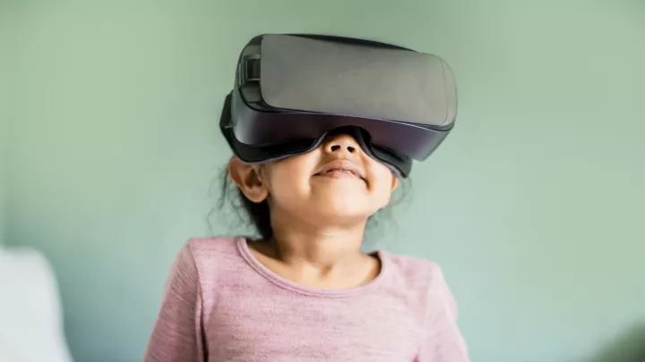 A little girl smiling, looking upward while wearing a VR headset.