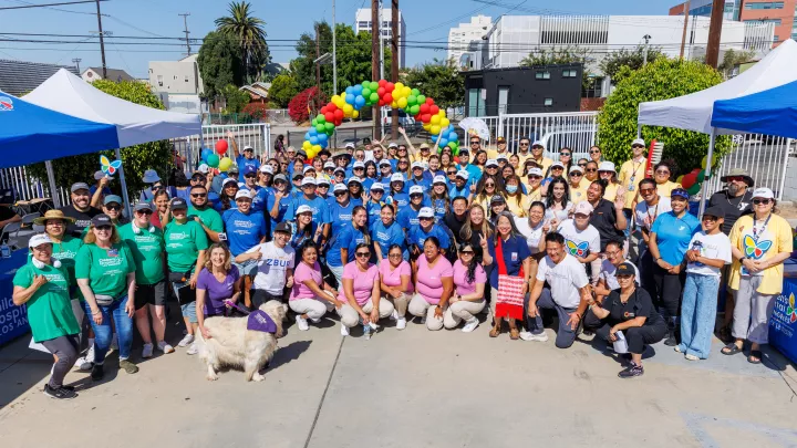 Large group of people gathered together in public space with arch of balloons in background