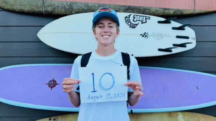 Smiling teenage boy with light skin tone holds up sign marking his first day of 10th grade