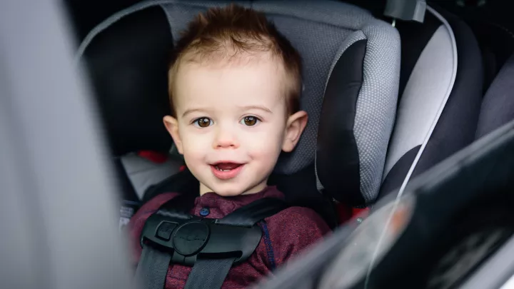 Toddler boy with light skin sitting in car seat with 5-point harness