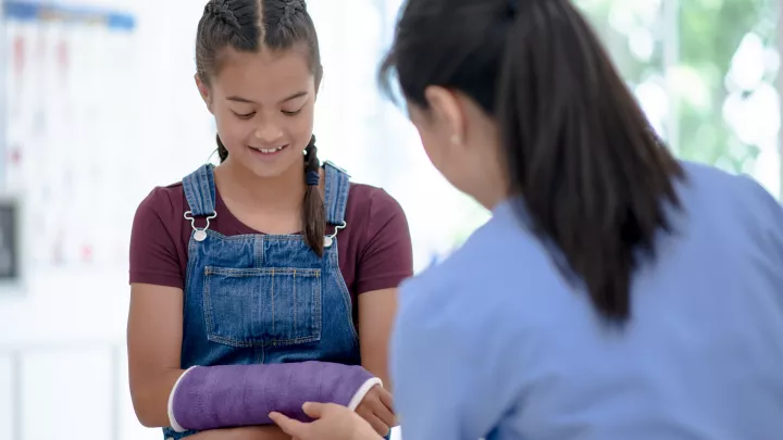 Adolescent girl in overalls and pigtails wearing purple cast on right arm