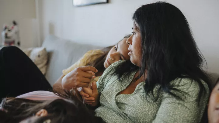 A mother comforts two of her children while they snuggle on the couch.