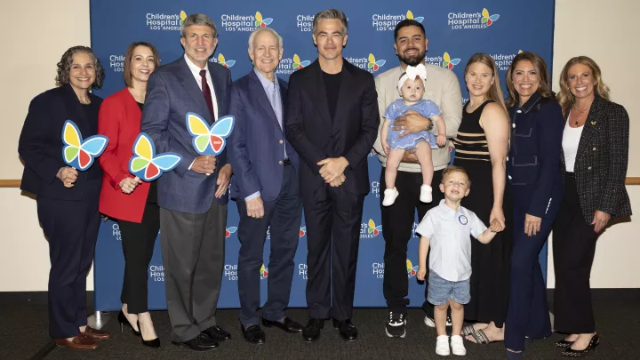 Actor Chris Pine is flanked by Children's Hospital Los Angeles executives and patient families wearing business attire and holding brightly colored CHLA butterfly cutouts