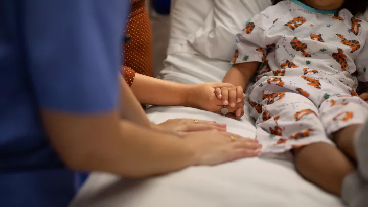 A young patient wearing a tiger print hospital gown holds the hands of their care team. 