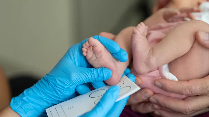 blue gloved hand measures infant foot