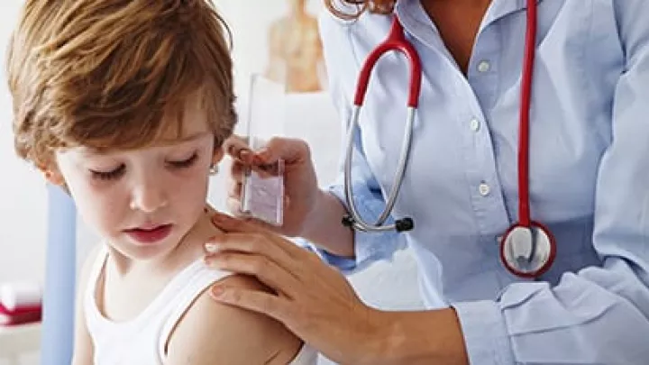 A doctor wearing a blue button down shirt and red stethoscope examans a young boy's shoulder.