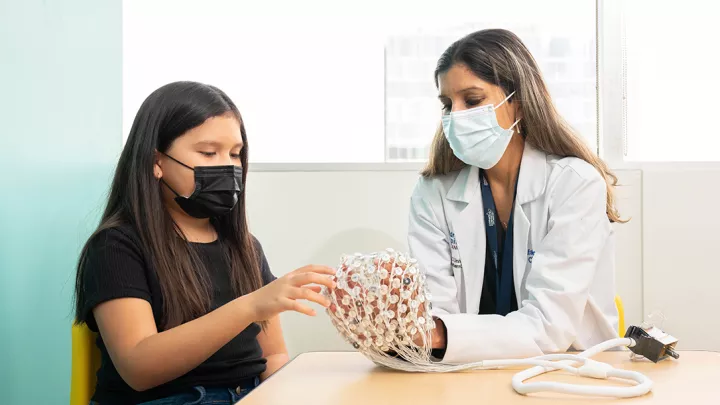 A girl and doctor both wearing medical procedure masks examine a model of a human brain.