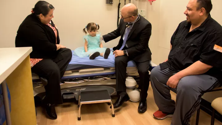 A young girl, Angelique Garcia, sits in a doctors office surounded by her parents and doctor.
