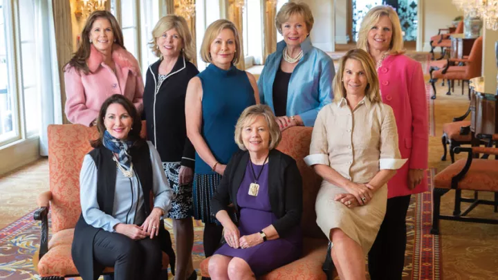 Eight women wearing business casual clothing smile and pose as a group.