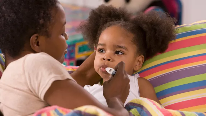 A woman takes a toddler's temperature with an oral thermometer.