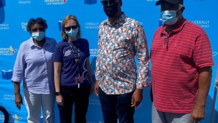 Four adults pose for a photo wearing medical procedure masks while standing in from of a blue wall.
