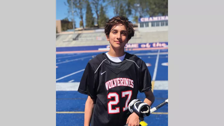Teen with light skin tone and brown hair wearing his lacrosse uniform standing on a stadium field