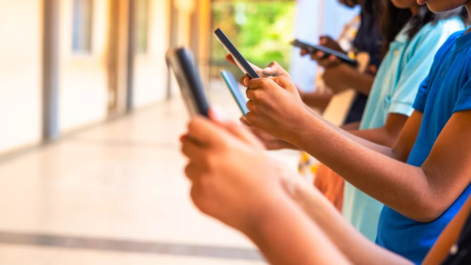 Three kids standing in a line, each holding a smartphone in their hands.