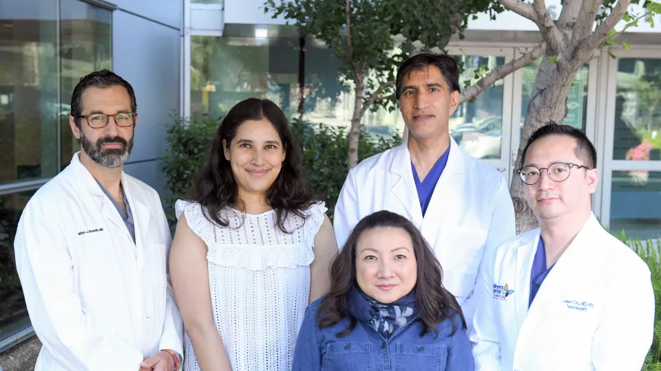 Three male researchers wearing white lab coats pose with two female researchers wearing business attire