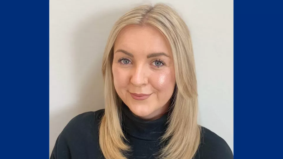 Headshot of a smiling woman with light skin tone and blonde hair wearing a dark turtleneck sweater