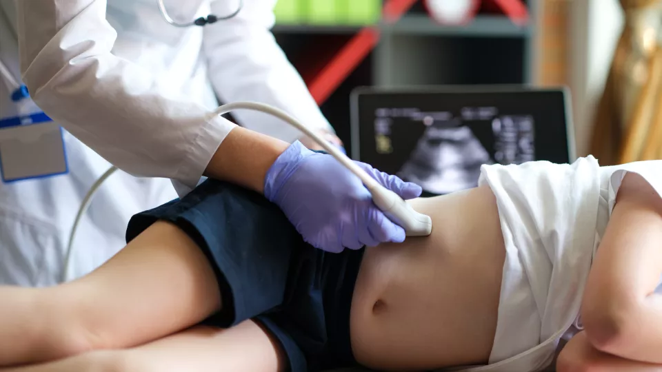 Doctor making examining with ultrasound of internal organs of child in clinic office