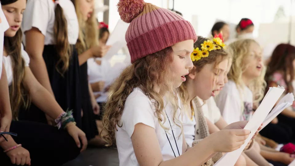 Young girls wearing white t-shirts sing from music sheets