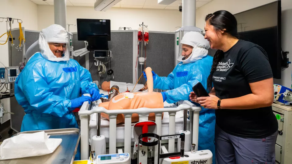 	Trainees in full HAZMAT suits work on medical mannequins in a simulated hospital room under the supervision on an instructor