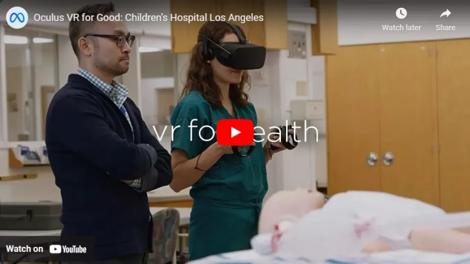 Screengrab of YouTube video player displaying trainee in operating scrubs using VR headset and controls in a medical simulation setting under the watchful eye of an instructor