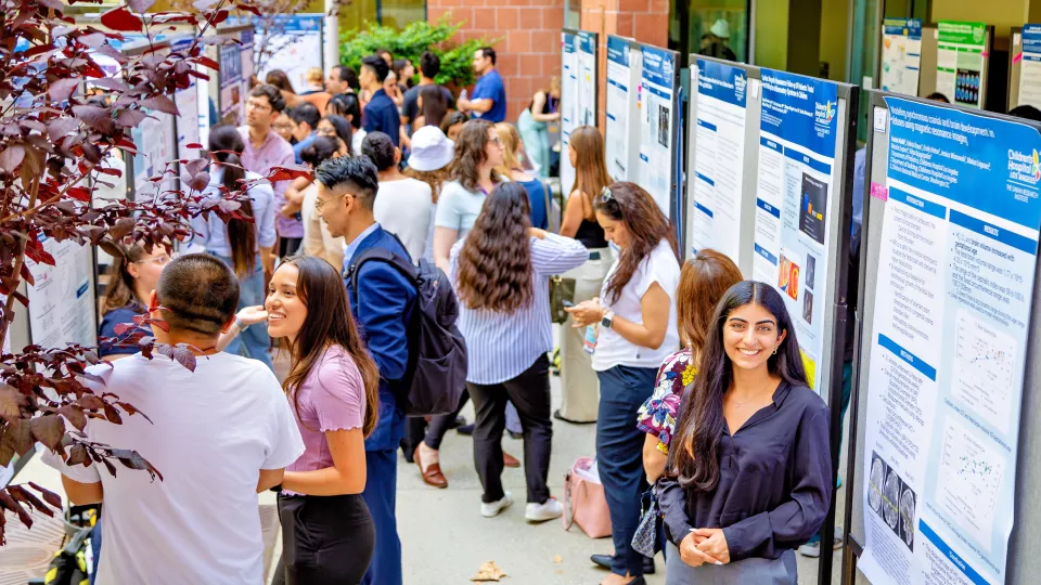 A crowd explores scientific research presentations at an outdoor poster session