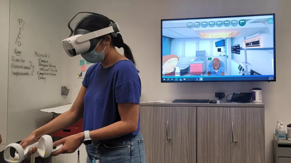 Masked female health care professional with medium skin tone and dark hair uses virtual reality controllers and headset
