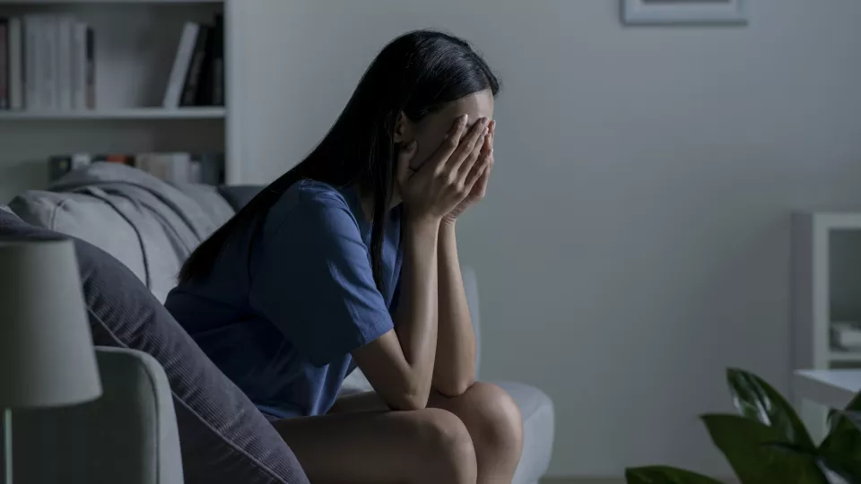 Young woman sitting on a sofa at home with her head in her hands.