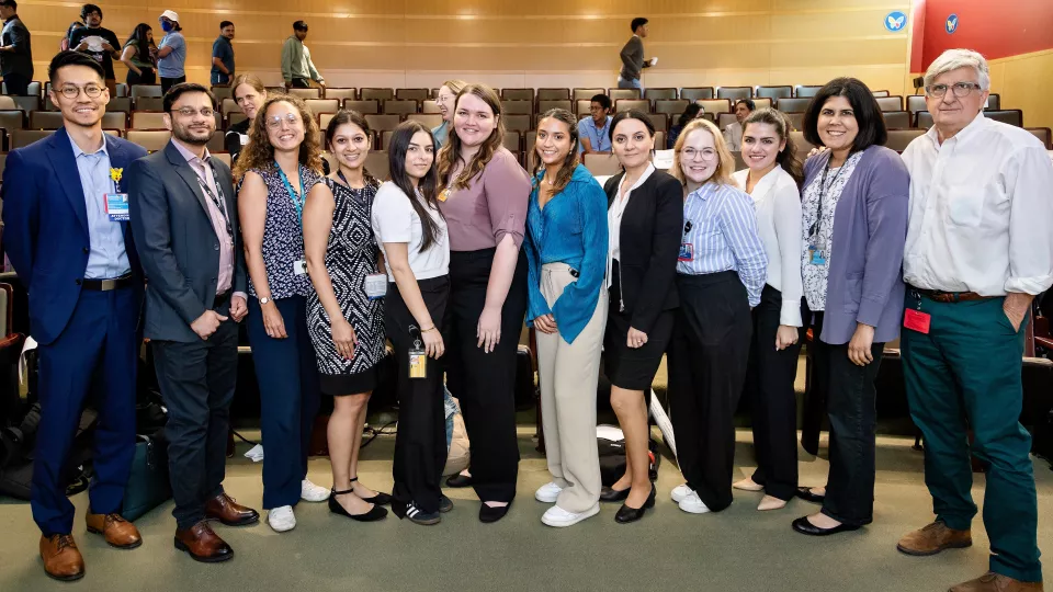 Group shot of 12 medical scientific researchers in formal attire posing together at the front of an auditorium.