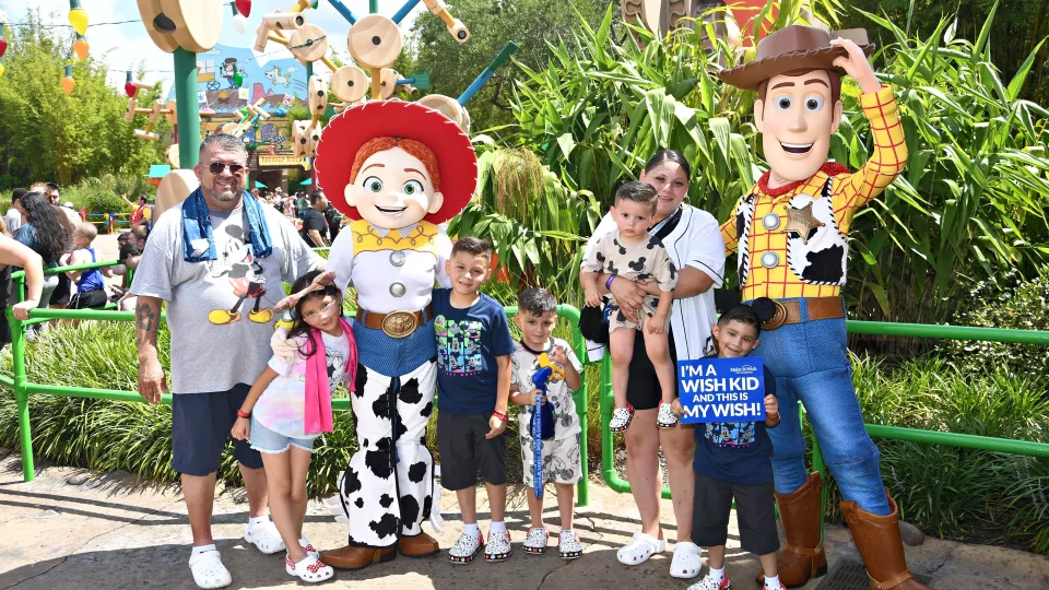 Nano, four of his siblings, and his mom and dad standing with two Toy Story characters at Disney World. 