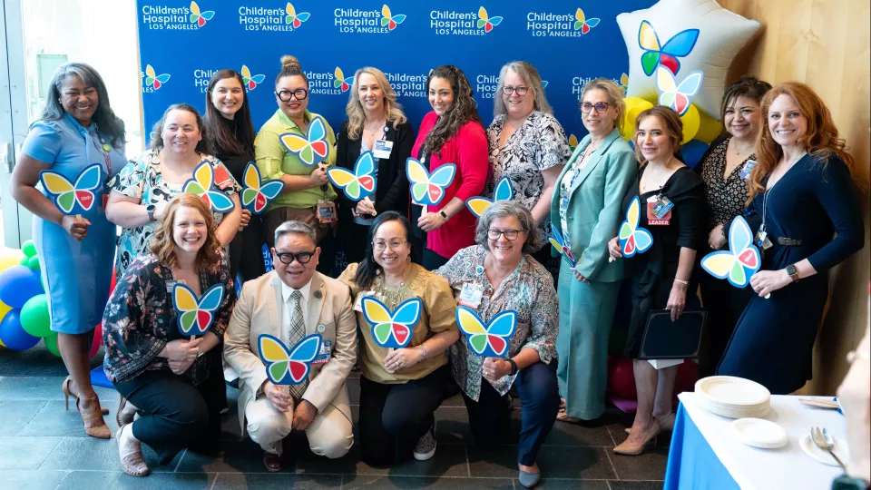 Group of women and men in two rows posing for team photo in front of CHLA-branded board