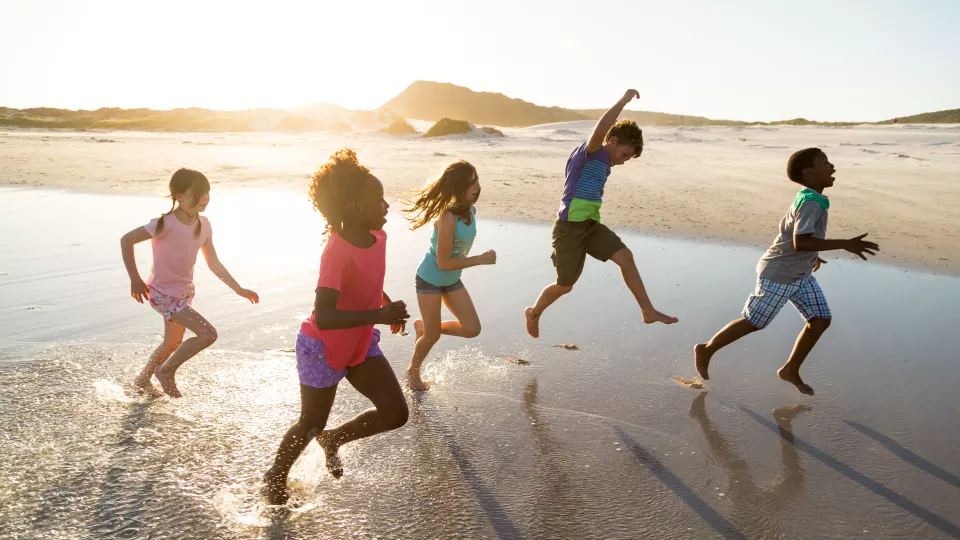 Five children running on a beach at sunset.