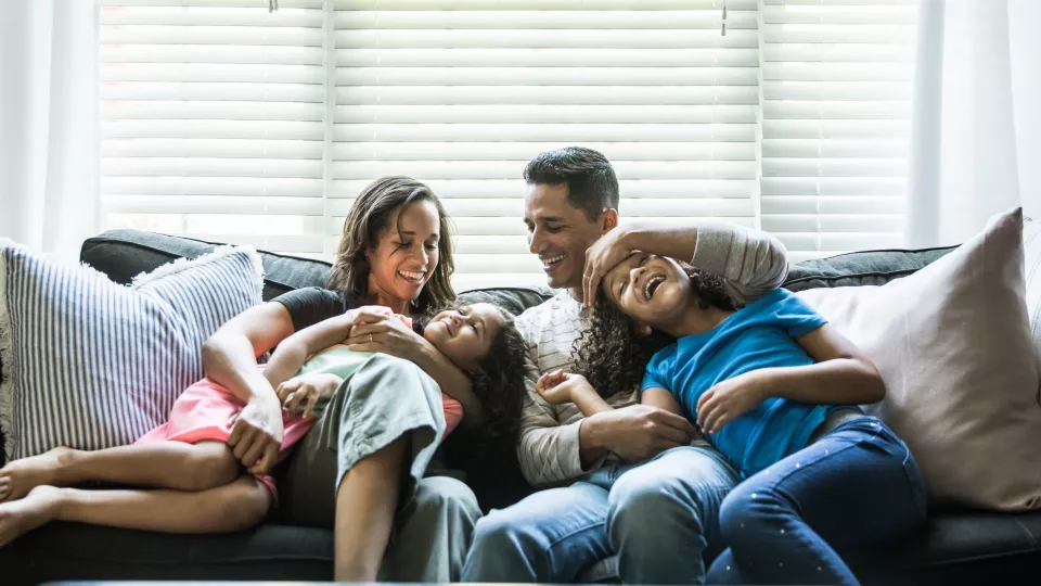 A family of four plays on their couch at home. 