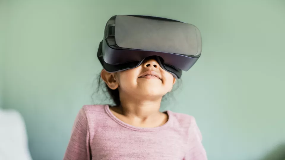 A little girl smiling, looking upward while wearing a VR headset.