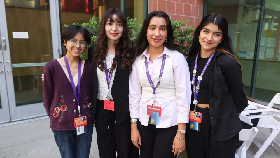 Four high school girls smile at the camera in an outdoor courtyard.