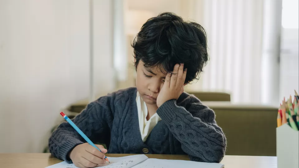 Young Asian child doing homework with hand on face