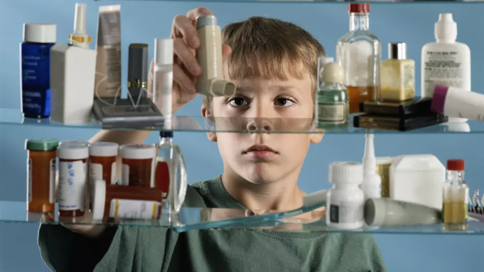 Young boy with light skin and light hair reaching for inhaler inside medicine cabinet