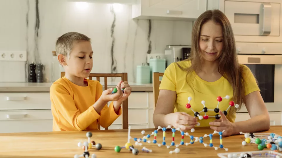 Young boy and mom play with a toy DNA model at the kitchen table.