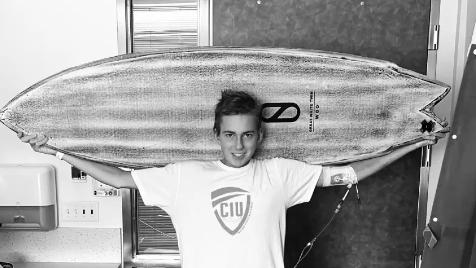 Smiling teenage boy holds surfboard behind his head