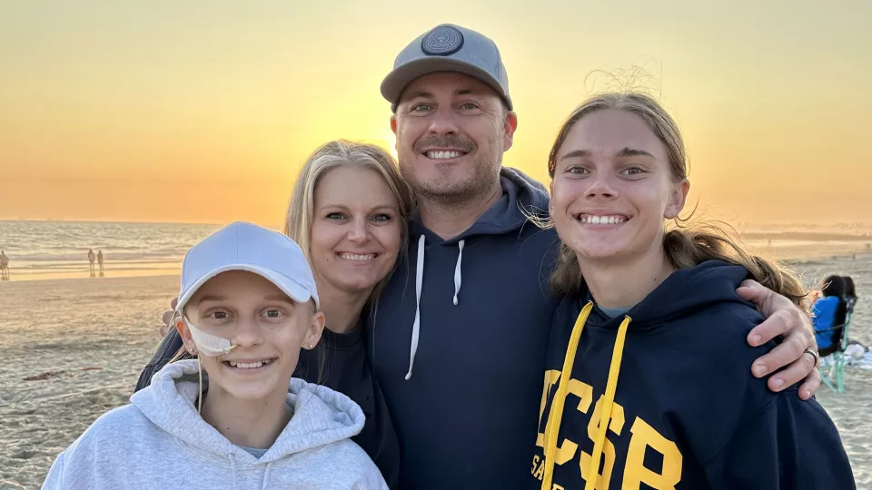 Four people with light skin standing on a beach side by side and smiling