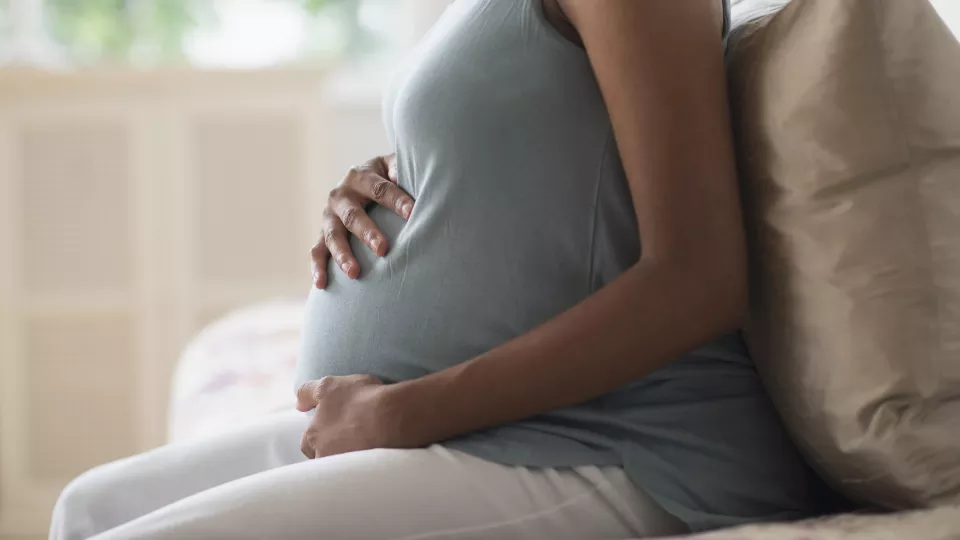 A pregnant woman holds her belly while sitting on a couch. 