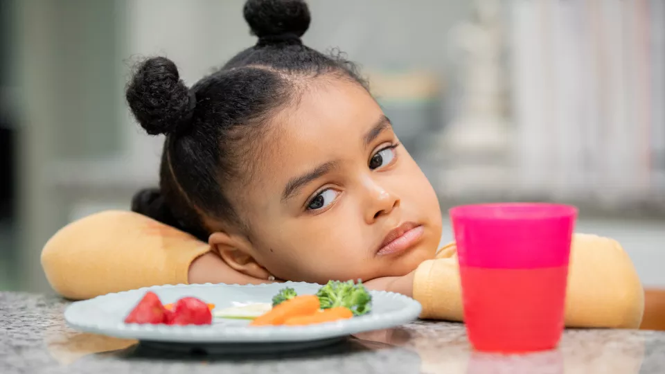 Small girl resting head on folded arms showing disinterest in plate of food