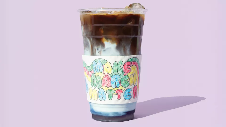 A cup of iced coffee with milk in a cup sleeve with the words Make March Matter in colorful lettering placed on a lavender background