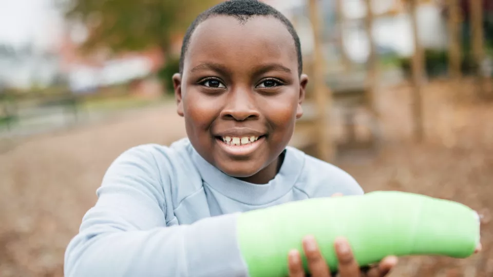 Child with dark skin and gray shirt wearing cast on right arm