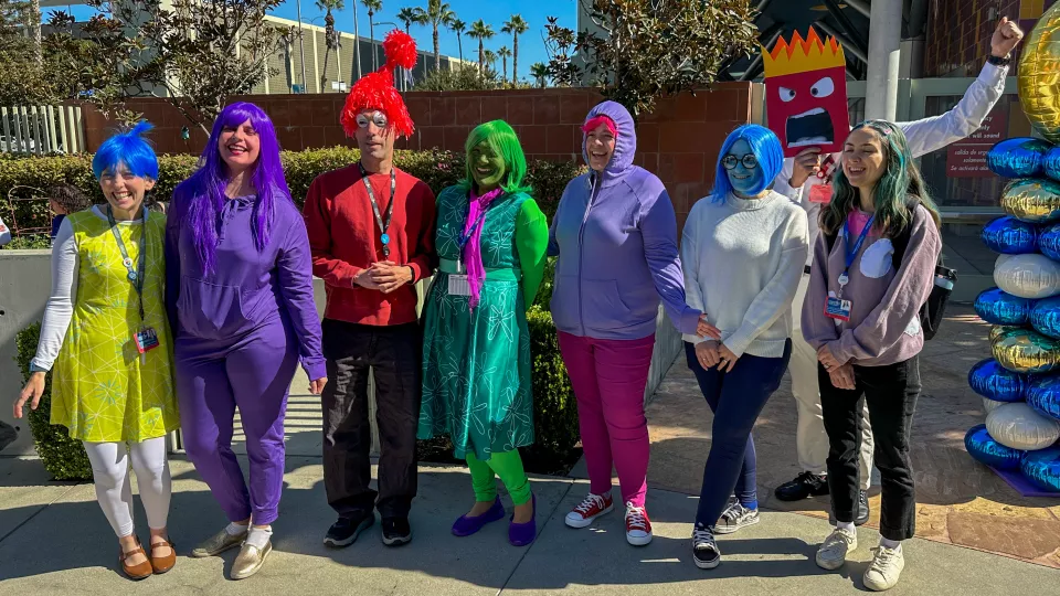 Eight team members dressed as characters from Pixar's Inside Out pose together. 