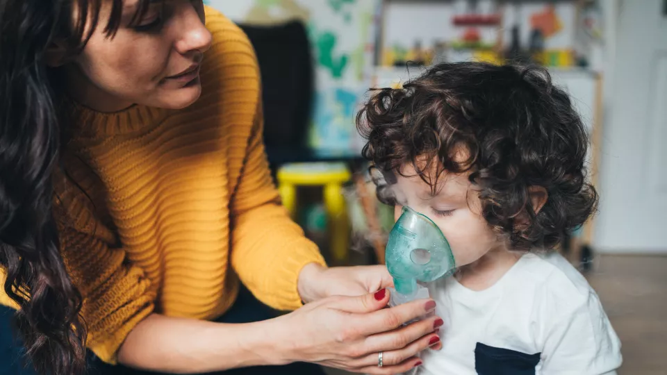 woman in yellow sweater helping child with brown curly hair with breathing mask