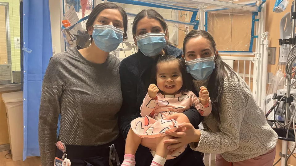 Baby smiling and held up by a happy trio of nurses