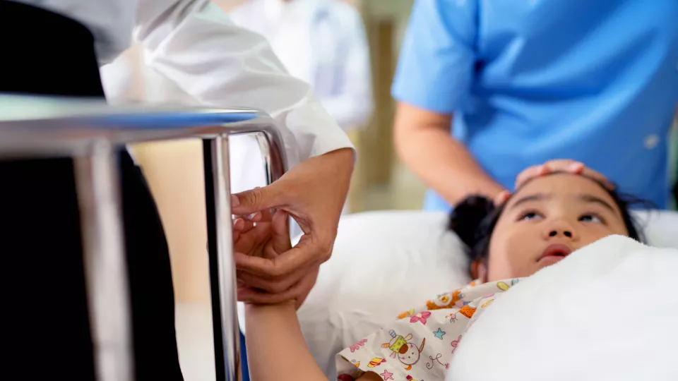 Asian young girl in hospital bed holding hands with adult