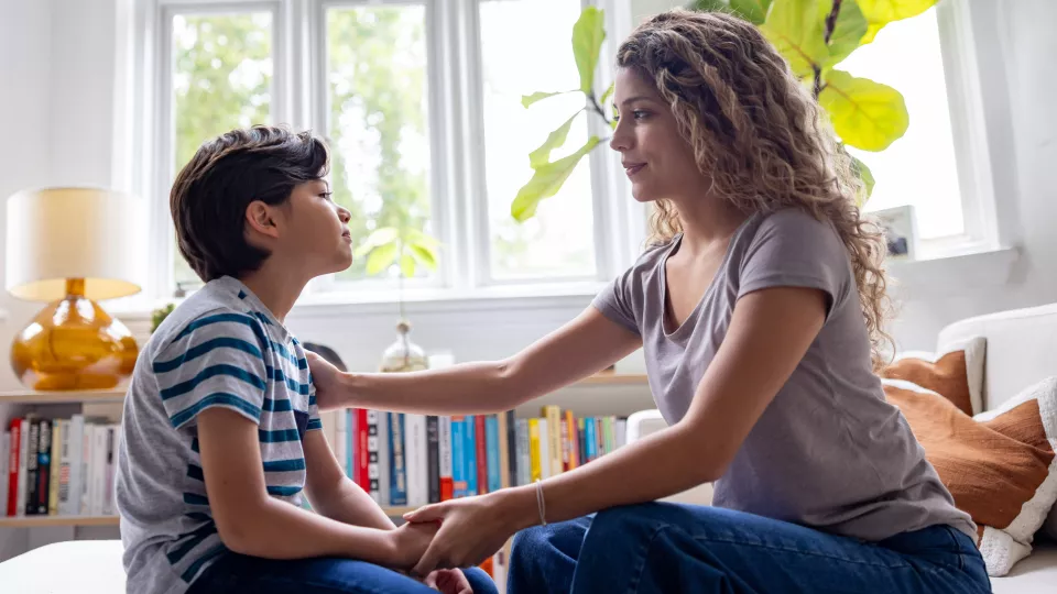 Mother with wavy hair places right arm on child's shoulder and holds his hand